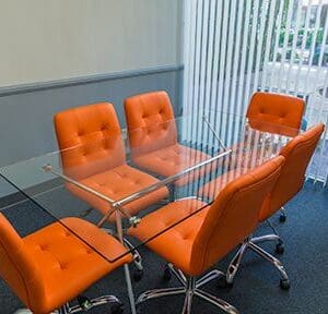 A glass table with orange chairs in front of it.